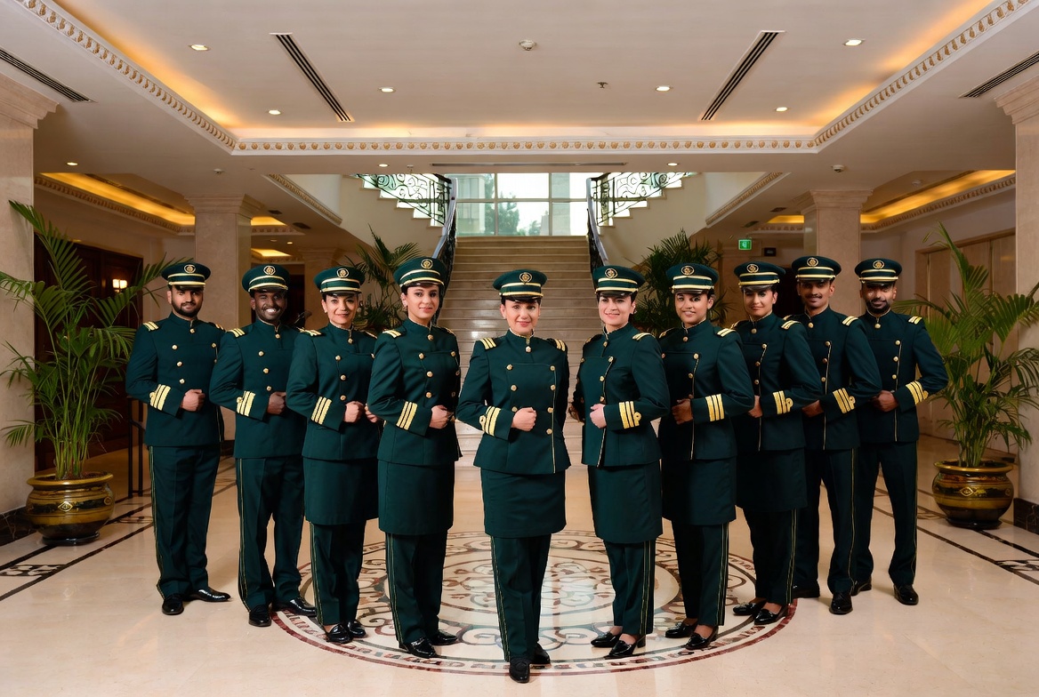 Confident team of hotel professionals wearing elegant dark green and gold ELEGANCE ATTIRE custom tailored uniforms in a luxury Muscat hotel lobby